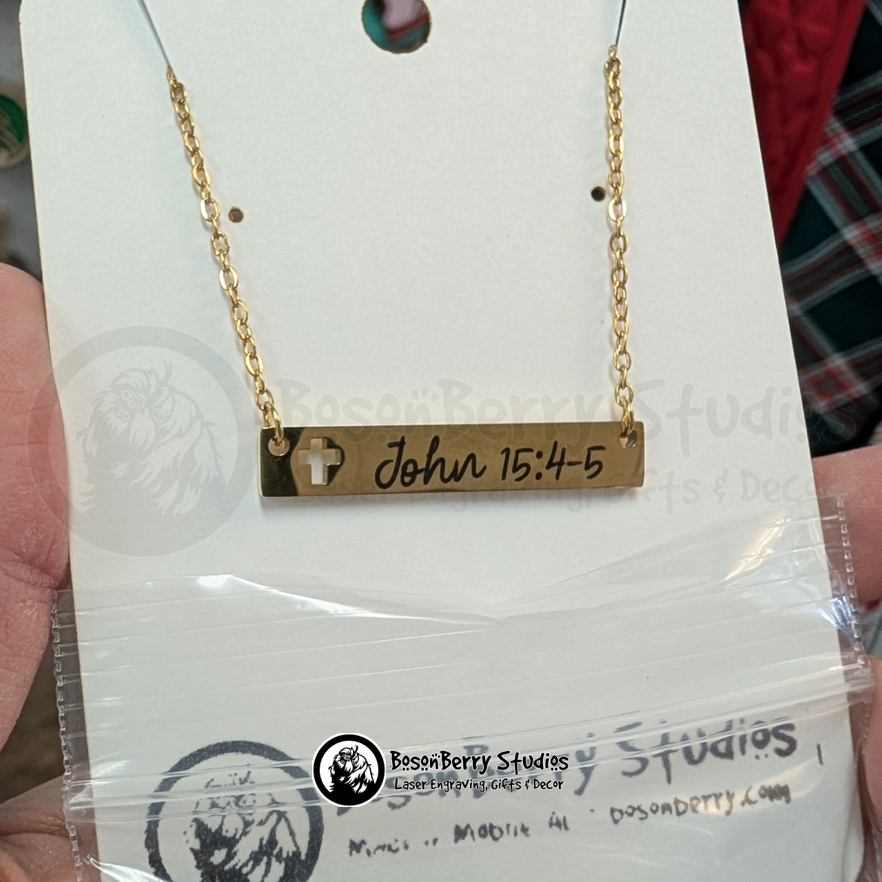 Gold necklace with bar pendant featuring a cross cutout, engraved with 'John 15:4-5' in a black, cursive font on a white jewelry display card, with 'BosonBerry Studios' branding.