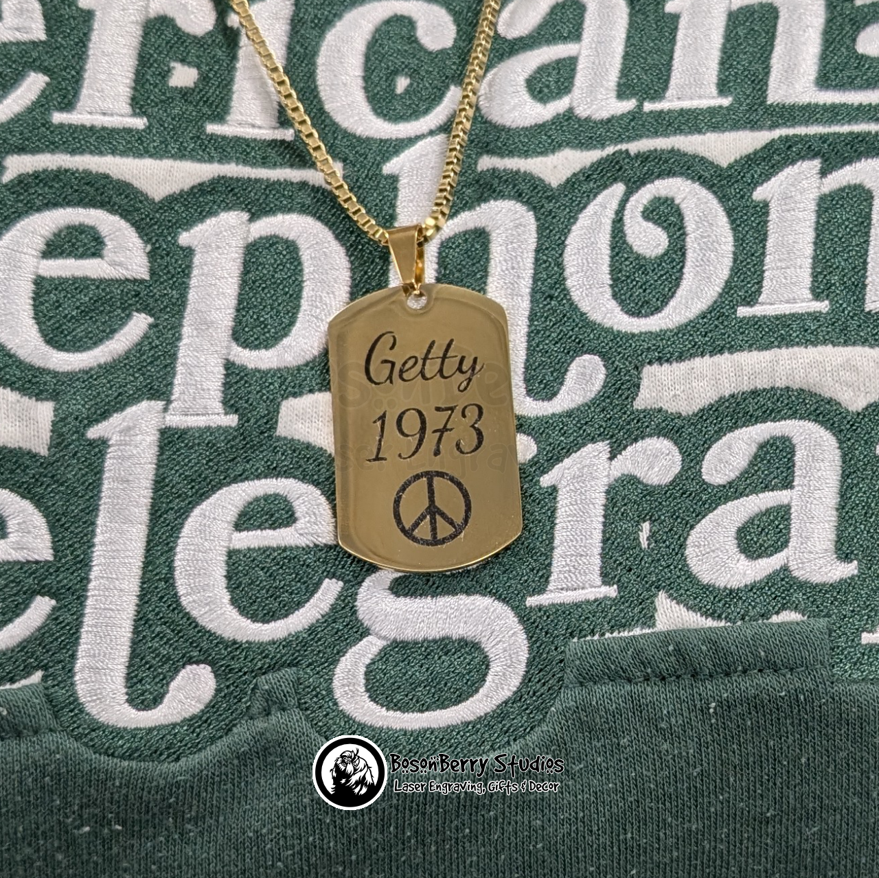 Gold necklace with a dog tag featuring 'Getty 1973' and a peace symbol on a green background with white text.