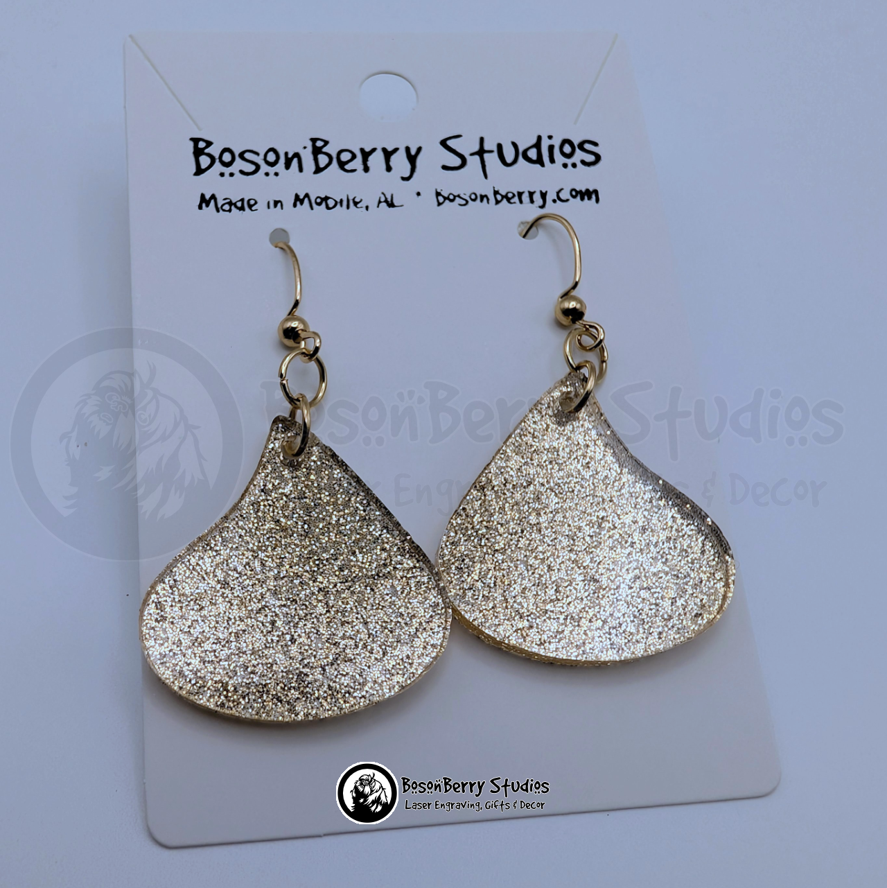 Gold glitter acrylic earrings shaped like wrapped chocolate candy drops, on display cards with 'BosonBerry Studios' branding.