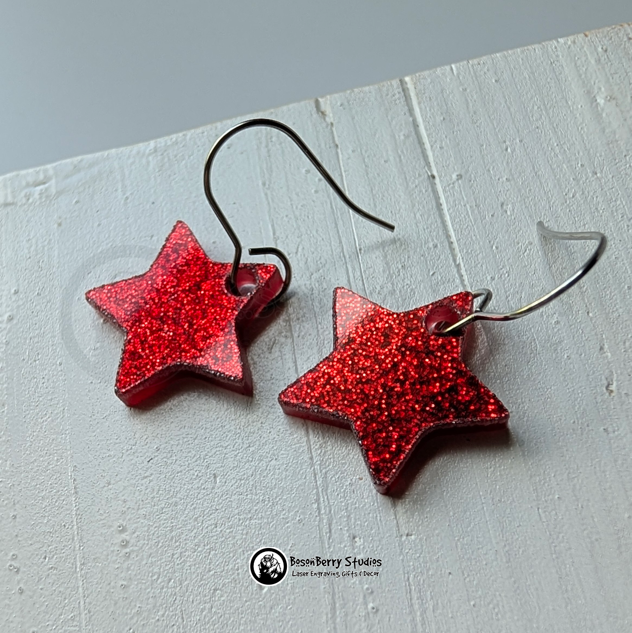 Star-shaped red glitter earrings on a white background, branded 'BosonBerry Studios'.