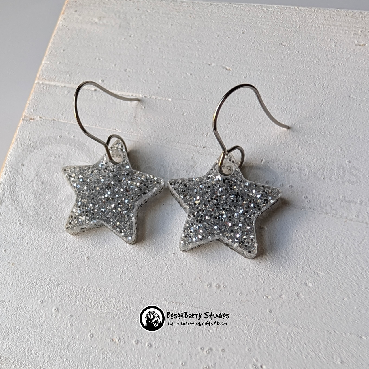 Star-shaped silver glitter earrings on a white background, branded 'BosonBerry Studios'.