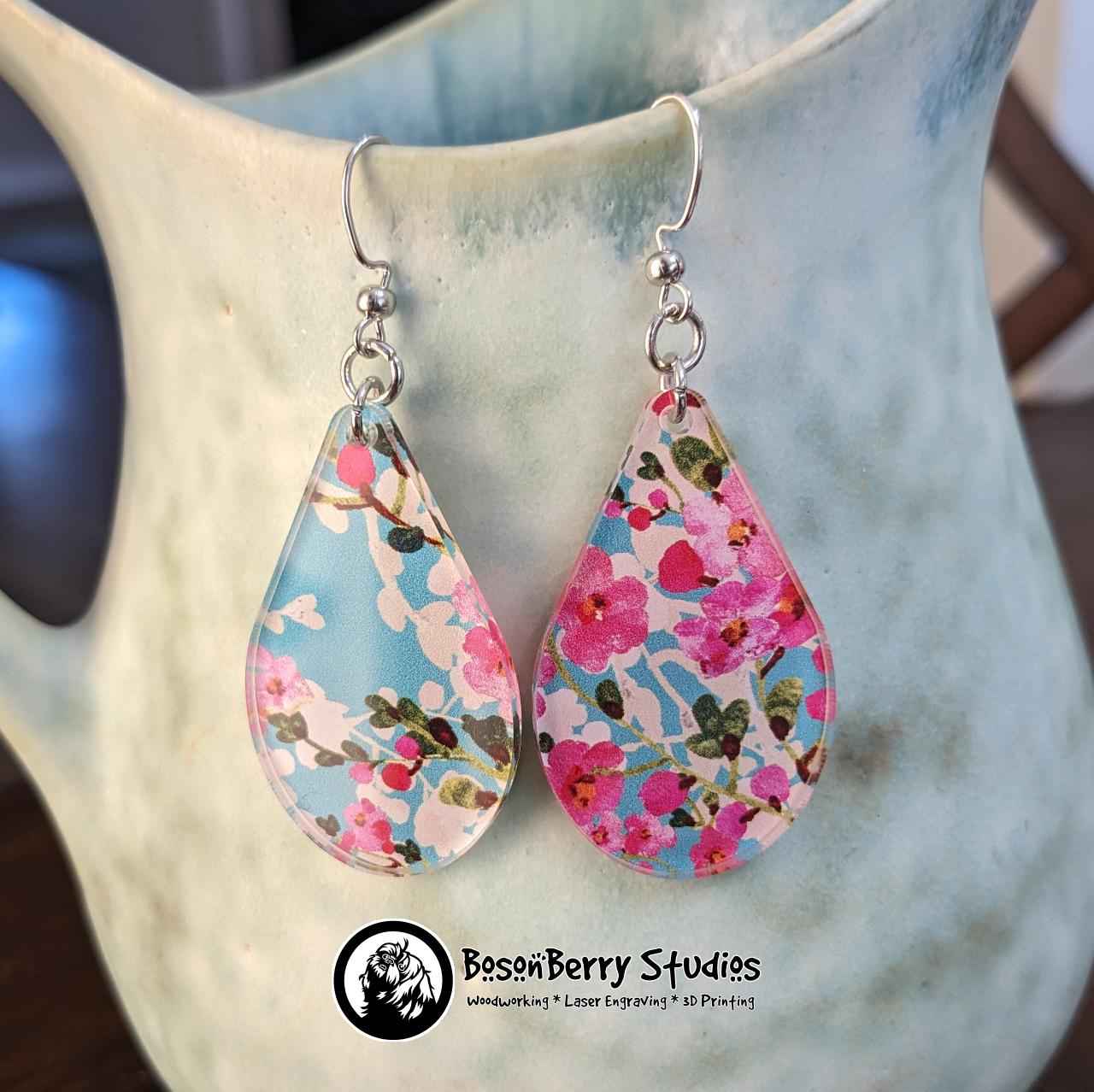 Teardrop shaped Cherry Blossom Acrylic Earrings hanging from a light blue-green ceramic pitcher.