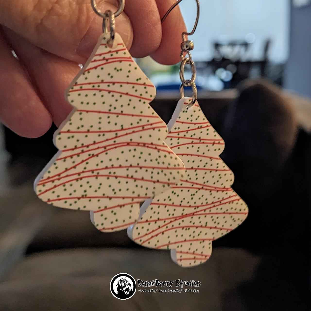 Christmas Snack Cake Acrylic Earrings shown held against a blurred background.
