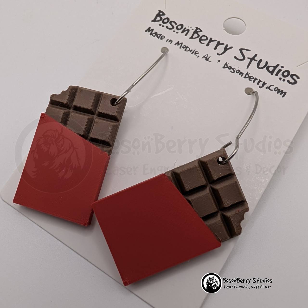 Set of brown chocolate bar-shaped earrings with red wrappers on cards with 'BosonBerry Studios' branding.
