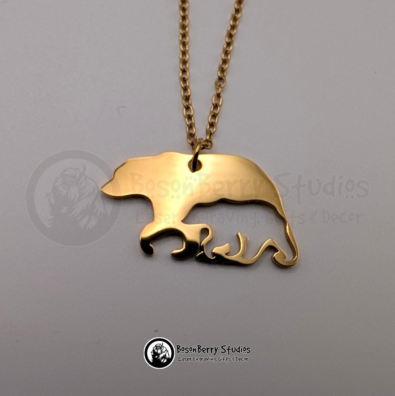 A gold bear-shaped pendant necklace with cub-shaped cutout on a white background with 'BosonBerry Studios' branding.