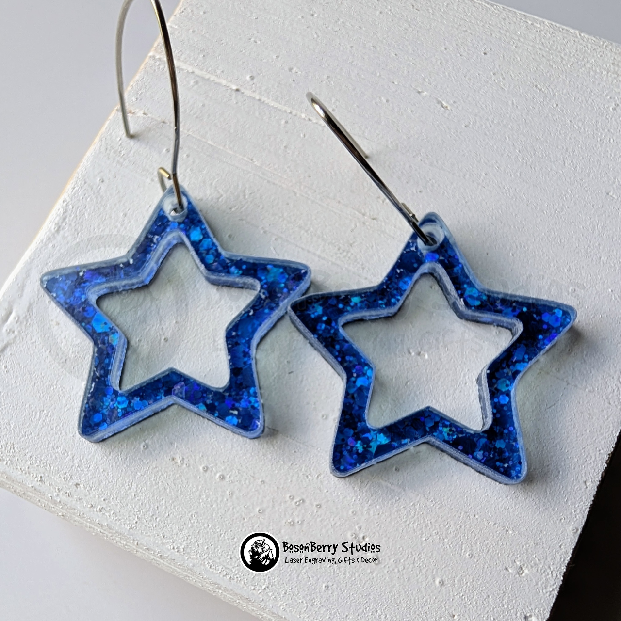 Star-shaped blue glitter earrings on a white background, branded 'BosonBerry Studios'.