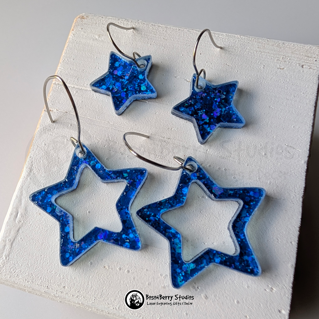 Star-shaped blue glitter earrings on a white background, branded 'BosonBerry Studios'.