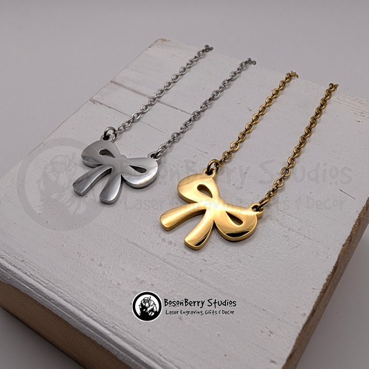 Two bow-shaped necklaces, one gold and one silver, on a white wooden stand with 'BosonBerry Studios' branding. 