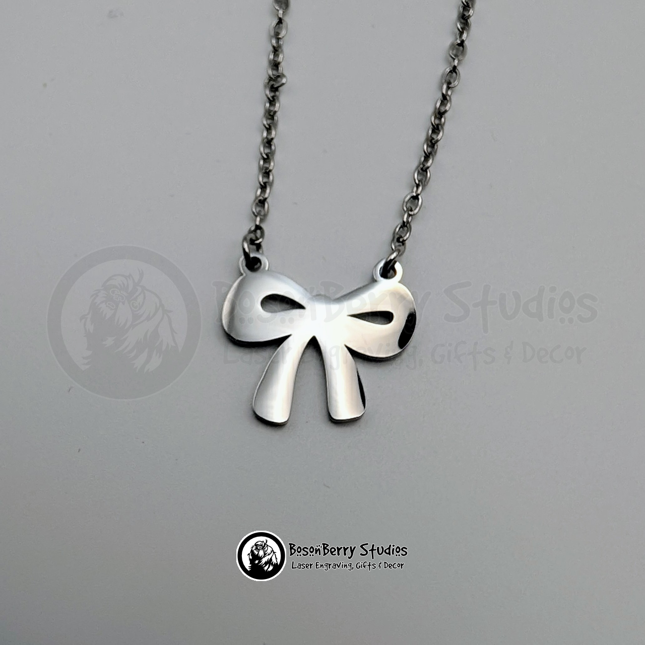 Silver bow-shaped pendant necklace on a white background with 'BosonBerry Studios' branding.