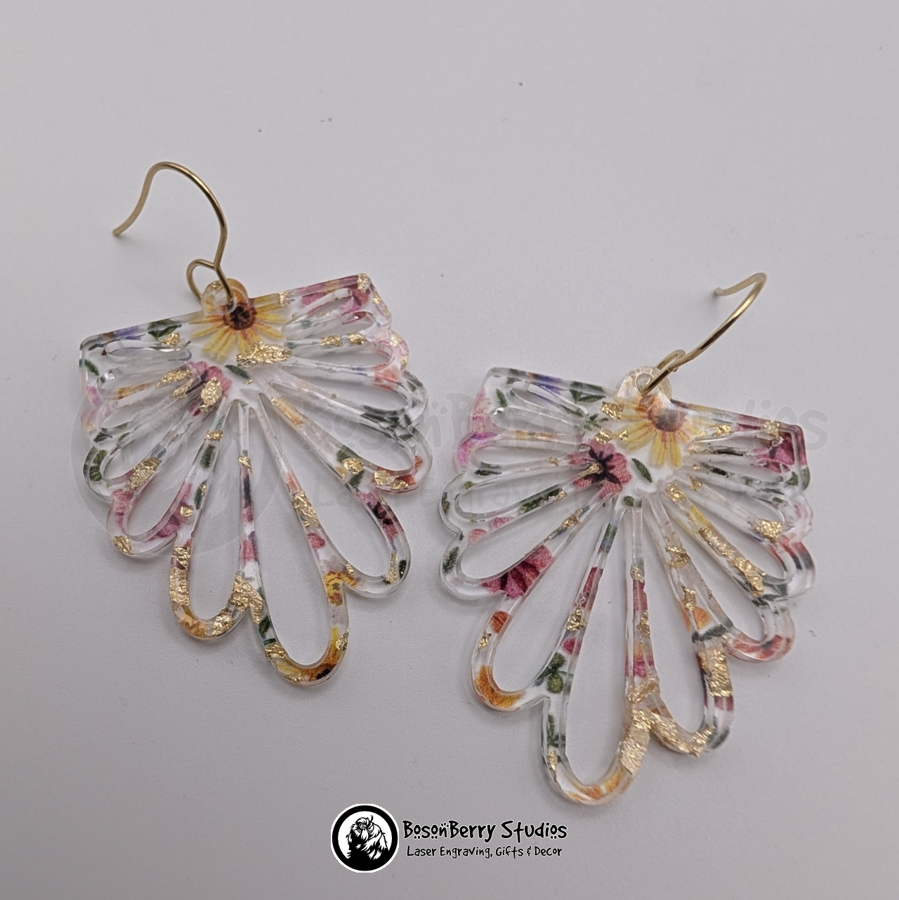 Clear acrylic earrings with embedded gold flakes and a multicolor floral print, in a floral petal burst half daisy shape, on a white background with 'BosonBerry Studios' branding.