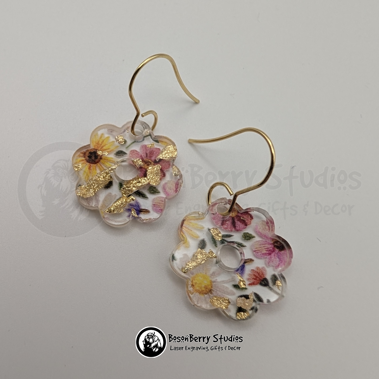 Clear acrylic earrings with embedded gold flakes and a multicolor floral print, in a tiny daisy shape, on a white background with 'BosonBerry Studios' branding.