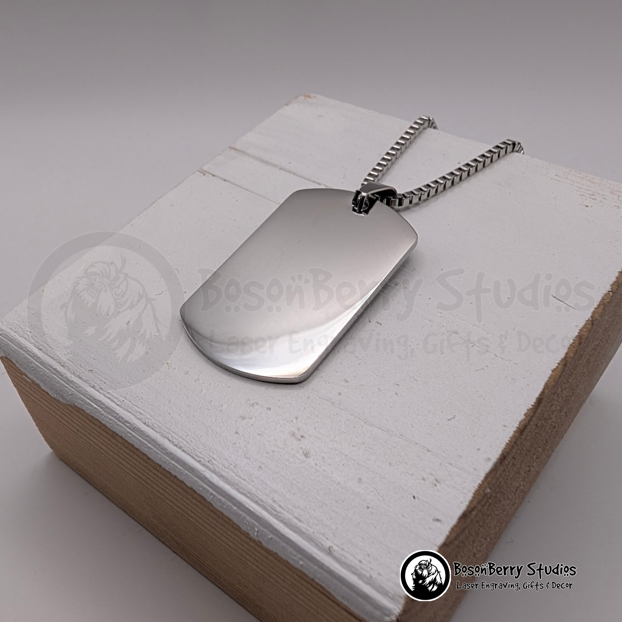 Silver dog tag pendant on a white wooden stand with 'BosonBerry Studios' branding.