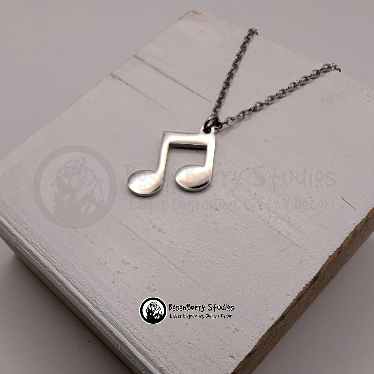 Silver music note pendant necklace on a white wooden stand with 'BosonBerry Studios' branding.