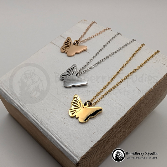 Butterfly-shaped pendants in rose gold, silver, and gold with matching necklace chains, displayed on a white wooden stand with 'BosonBerry Studios' branding.