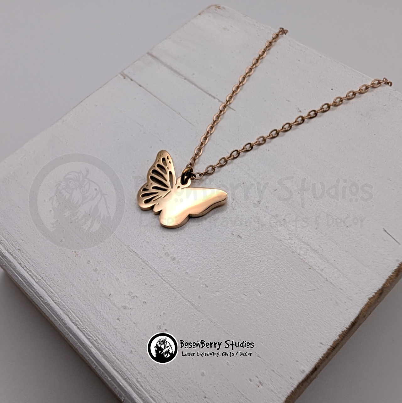 Rose Gold butterfly necklace on a white wooden stand with 'BosonBerry Studios' branding.