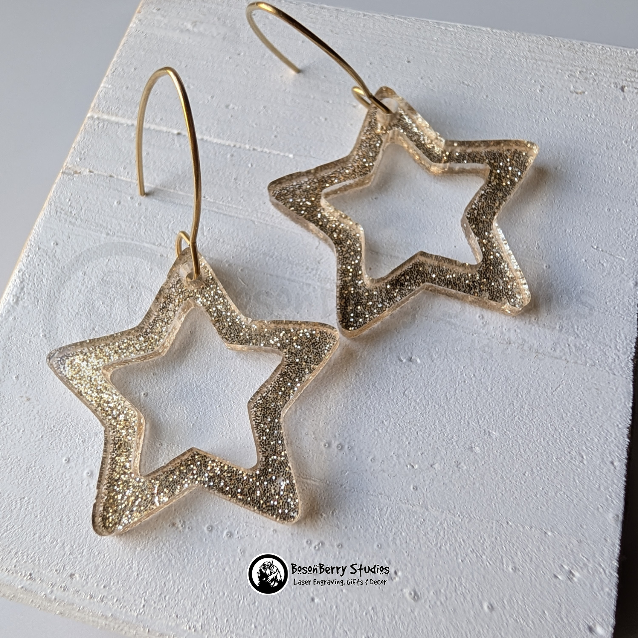 Star-shaped gold glitter earrings on a white background, branded 'BosonBerry Studios'.