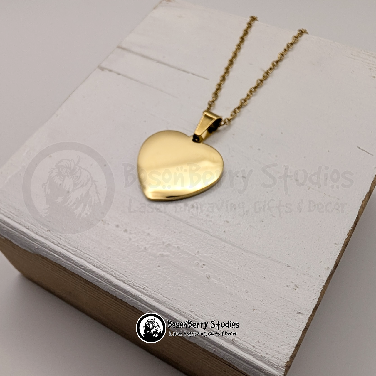 Gold heart-shaped pendant necklace on a white wooden stand with 'BosonBerry Studios' branding.