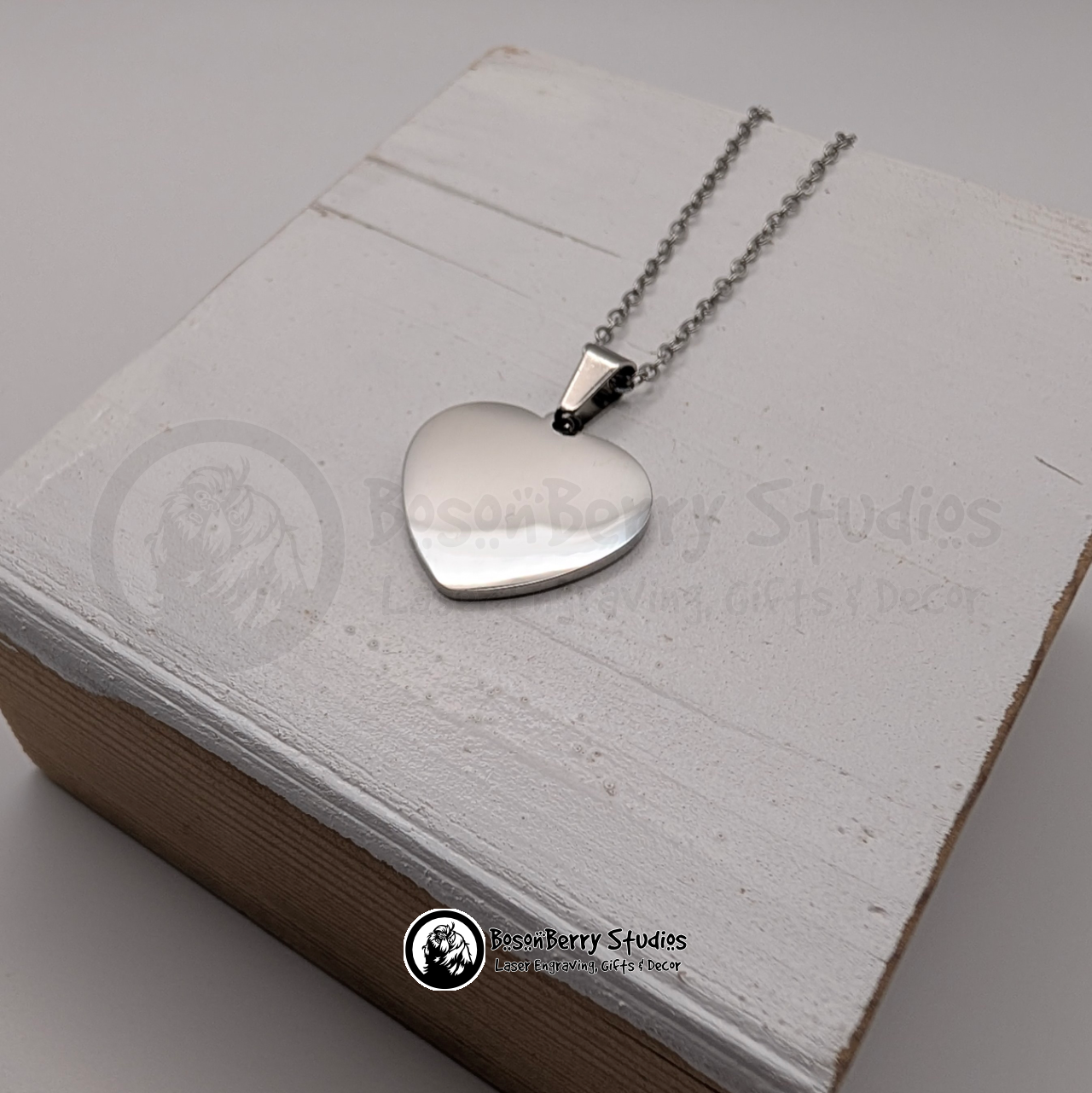 Silver heart-shaped pendant necklace on a white wooden stand with 'BosonBerry Studios' branding.