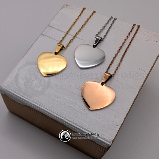 Trio of heart-shaped pendant necklaces, gold, silver, and rose gold, on a white wooden stand with 'BosonBerry Studios' branding.