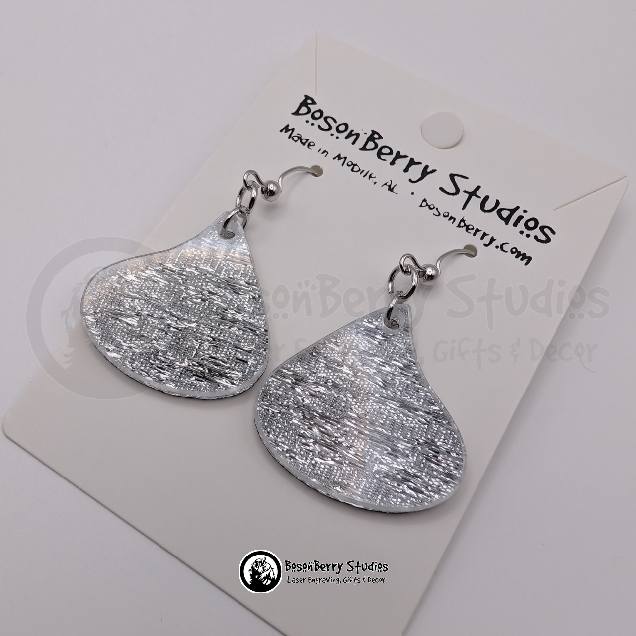 Silver metallic acrylic earrings shaped like wrapped chocolate candy drops, on display cards with 'BosonBerry Studios' branding.