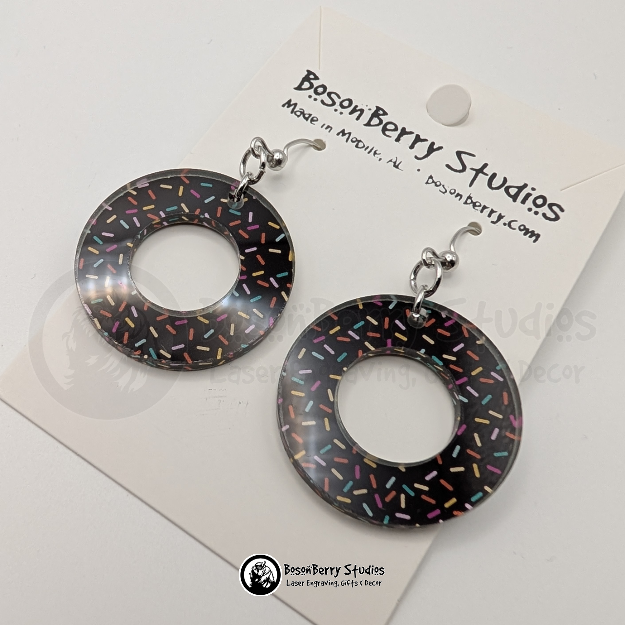 Large chocolate donut-shaped acrylic earrings, with a colorful sprinkle pattern, on a BosonBerry Studios card.