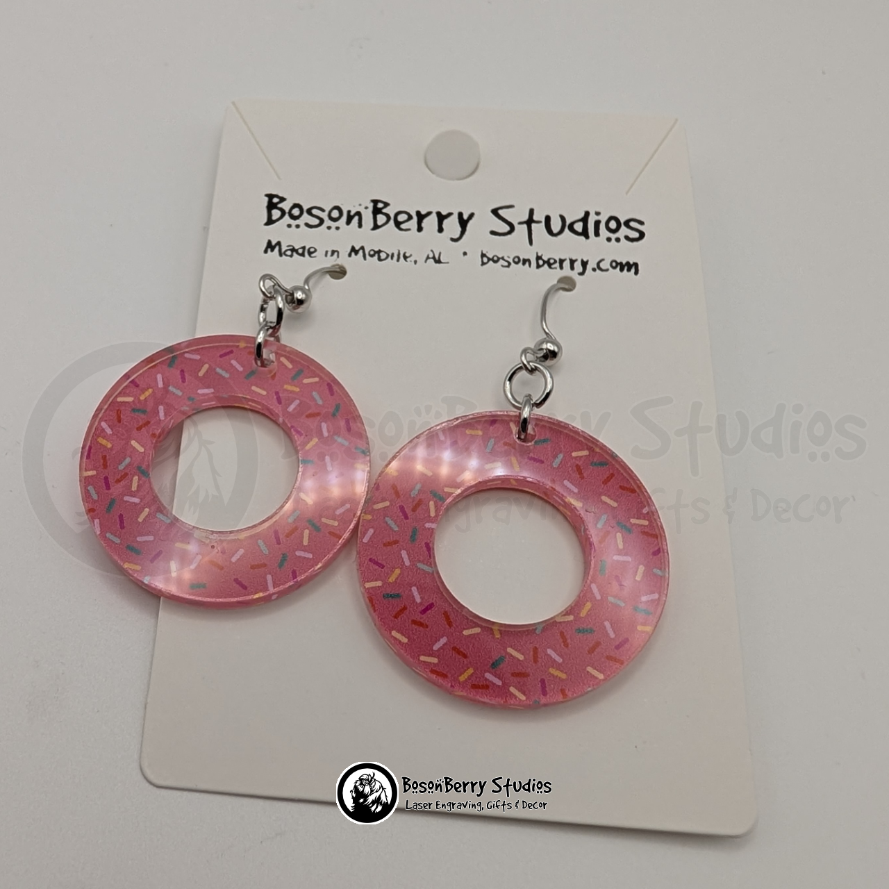 Large pink donut-shaped acrylic earrings, with a colorful sprinkle pattern, on a BosonBerry Studios card.