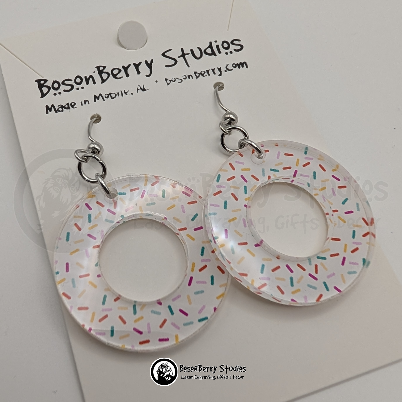 Large white donut-shaped acrylic earrings, with a colorful sprinkle pattern, on a BosonBerry Studios card.