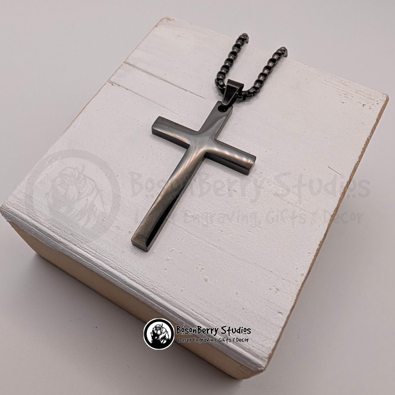 Black large cross pendant on a white wooden stand with 'BosonBerry Studios' branding.