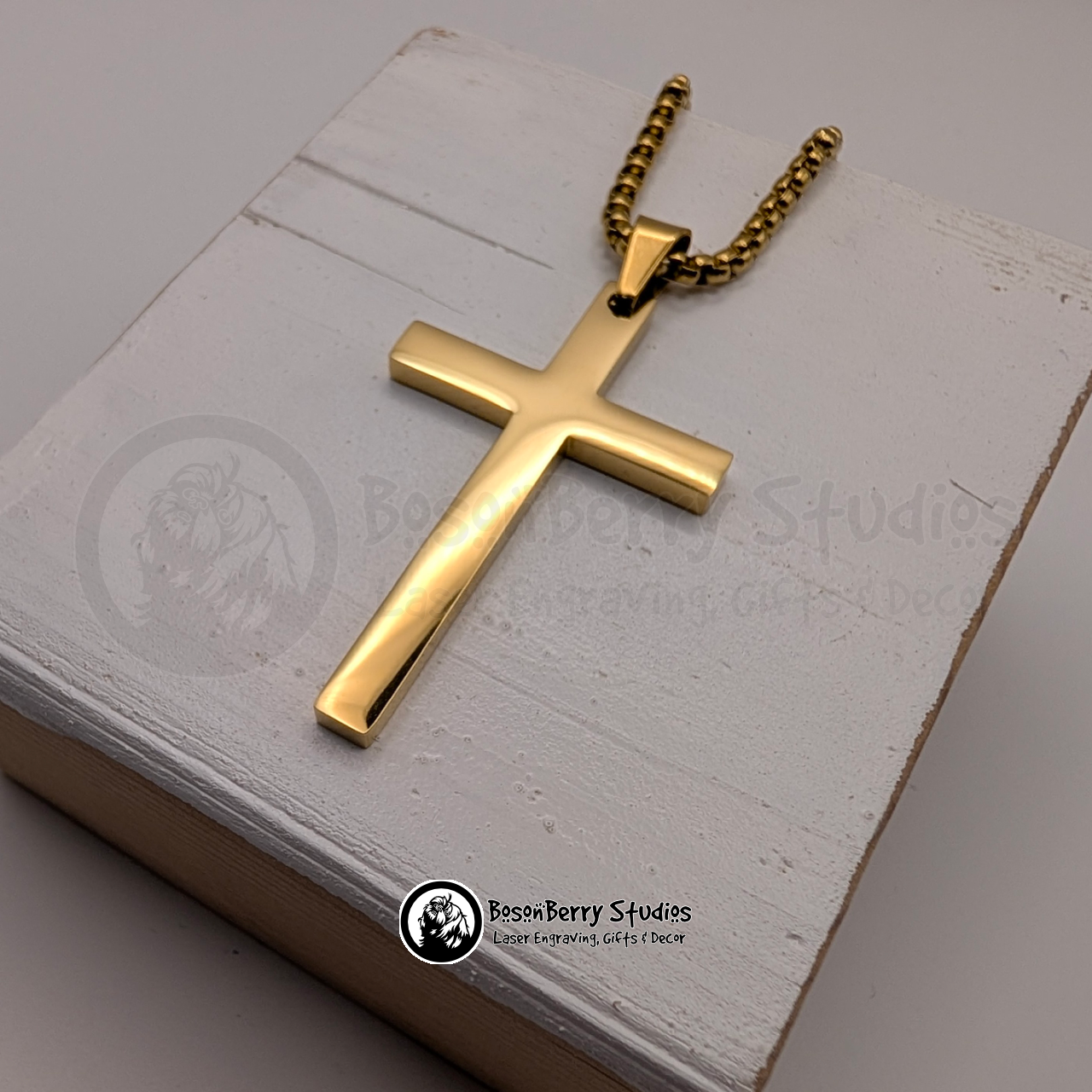 Gold large cross necklace on a white wooden stand with 'BosonBerry Studios' branding.