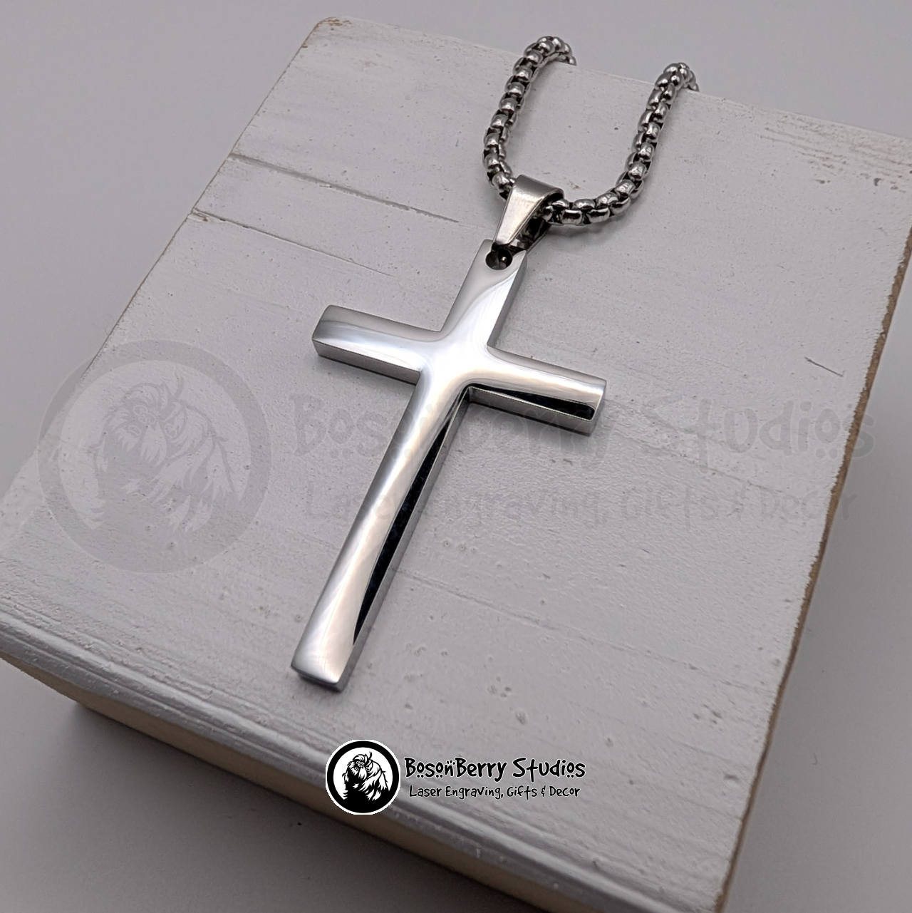 Silver large cross pendant on a white wooden stand with 'BosonBerry Studios' branding.