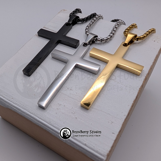 Three large cross pendants in black, silver, and gold on a white wooden stand with 'BosonBerry Studios' branding.