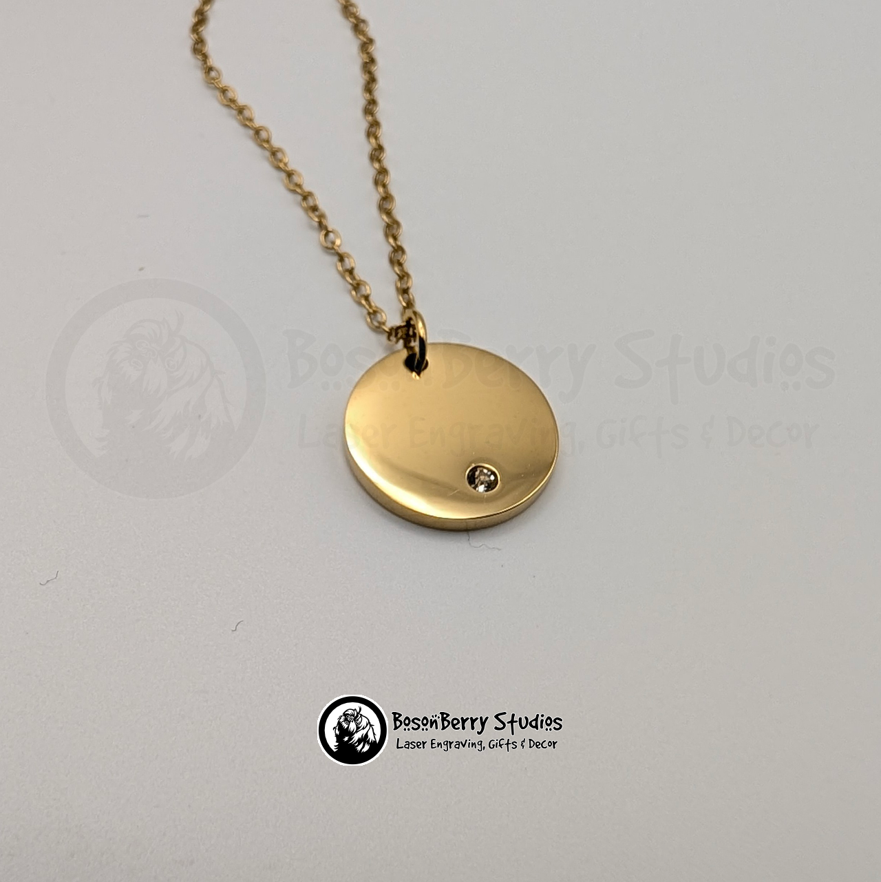 Gold necklace with a round pendant inset with a tiny cubic zirconia crystal on a white background with 'BosonBerry Studios' branding.