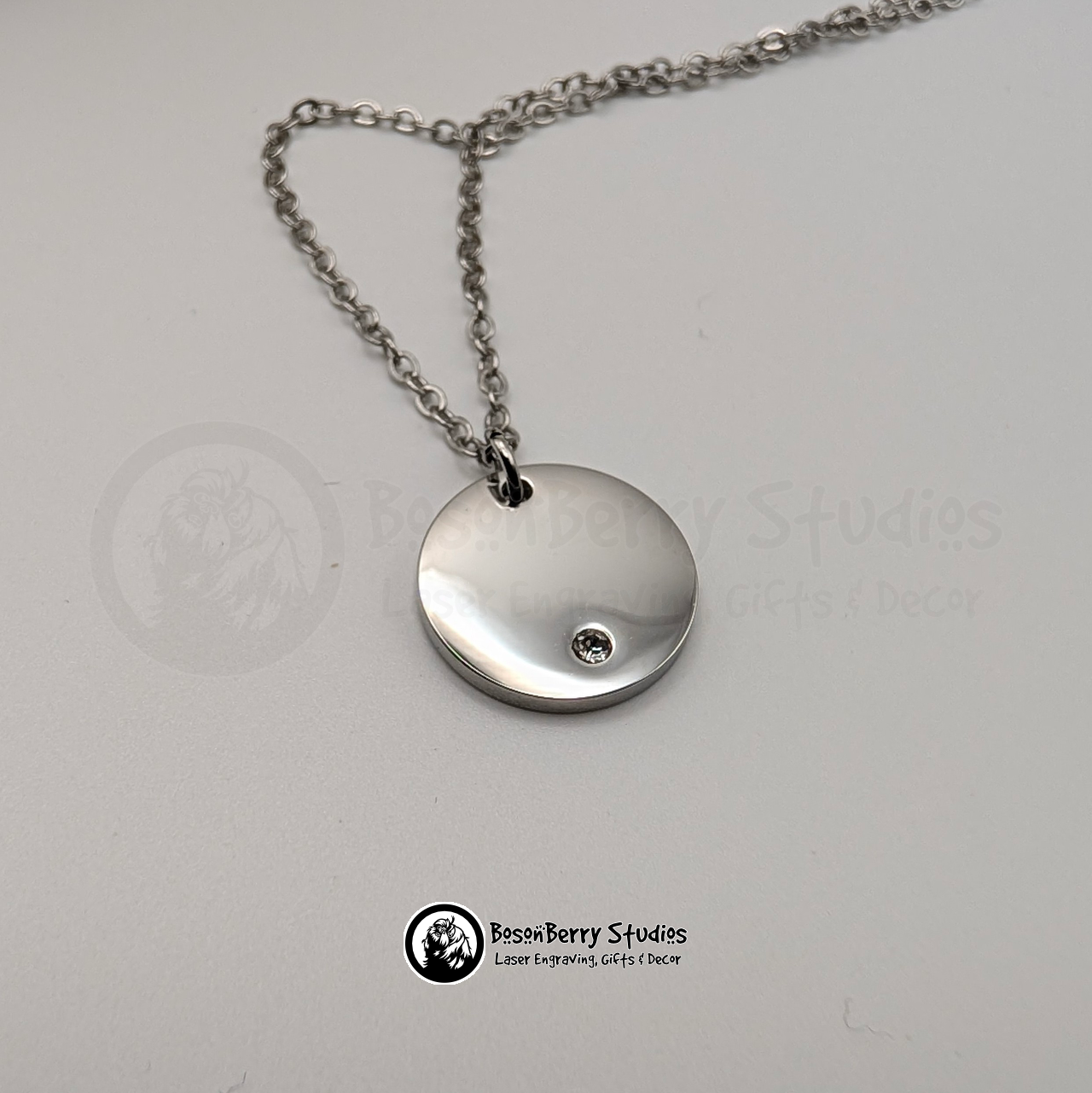 Silver necklace with a round pendant inset with a tiny cubic zirconia crystal on a white background with 'BosonBerry Studios' branding.