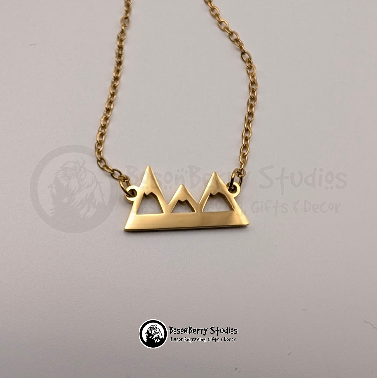 Gold necklace with mountain pendant on a white background with 'BosonBerry Studios' branding.