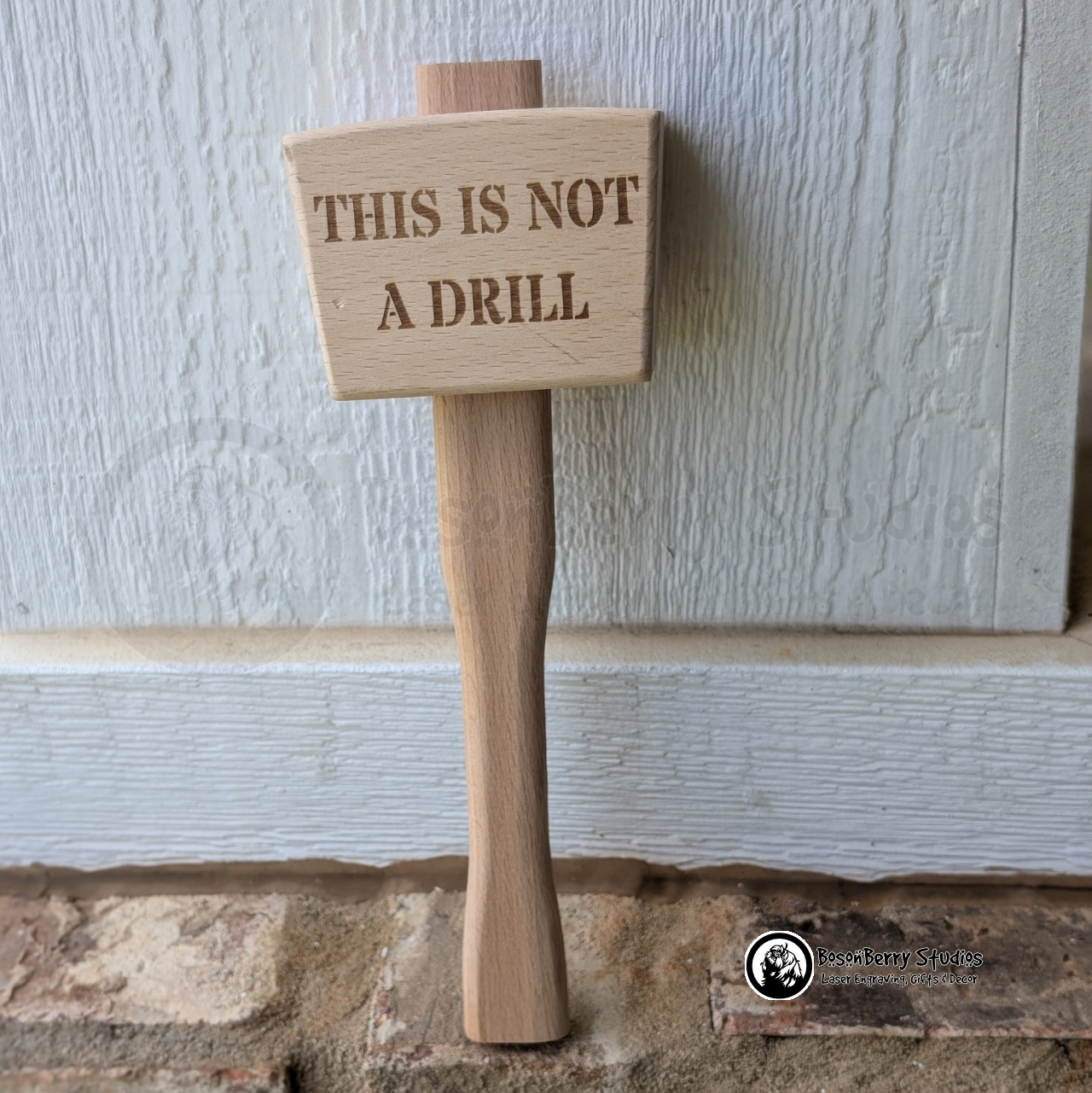 Wooden mallet engraved with 'This is not a drill' text on a stone surface against a white background.