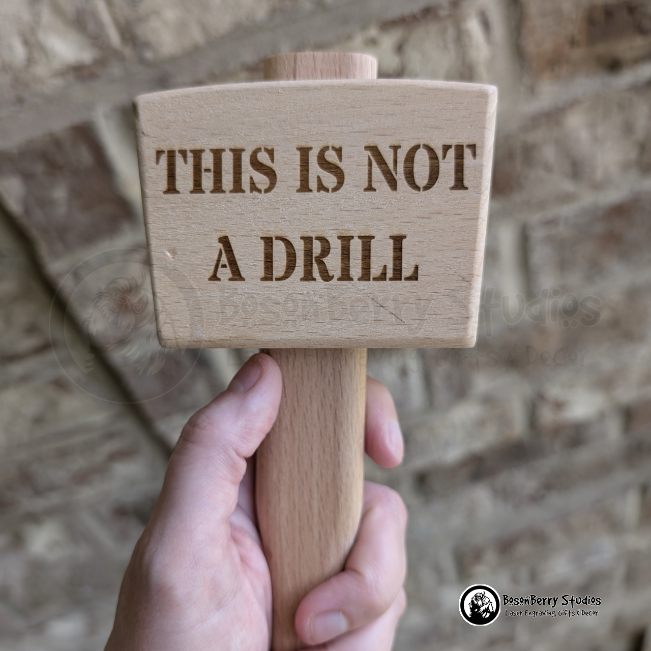 Wooden mallet engraved with 'This is not a drill' text held against a brick wall.