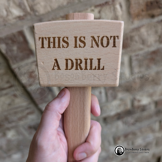 Wooden mallet engraved with 'This is not a drill' text held against a brick wall.