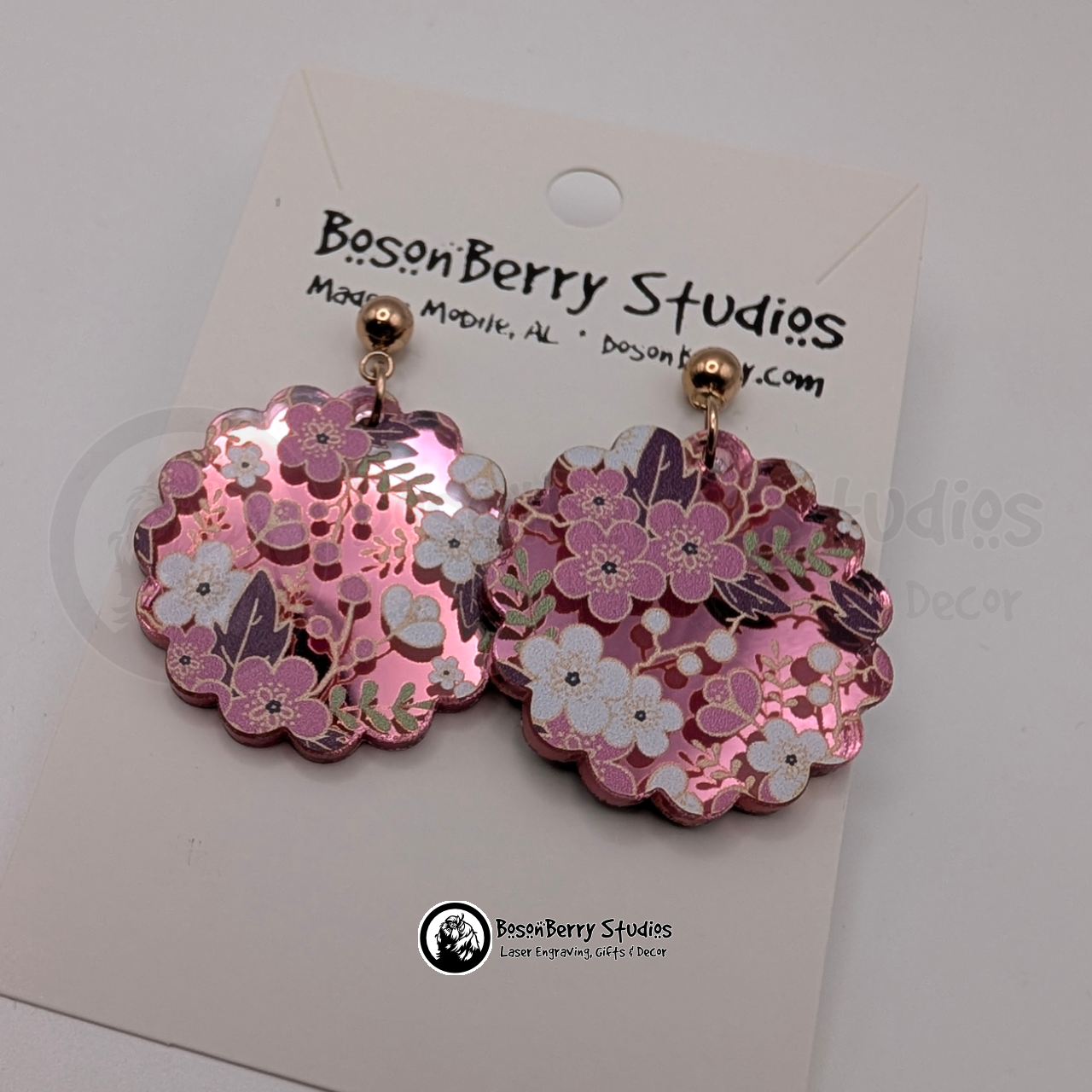 Earrings featuring a white and pink cherry blossom pattern on a pink mirrored acrylic field, in a scalloped circle shape, on display cards with 'BosonBerry Studios' branding.