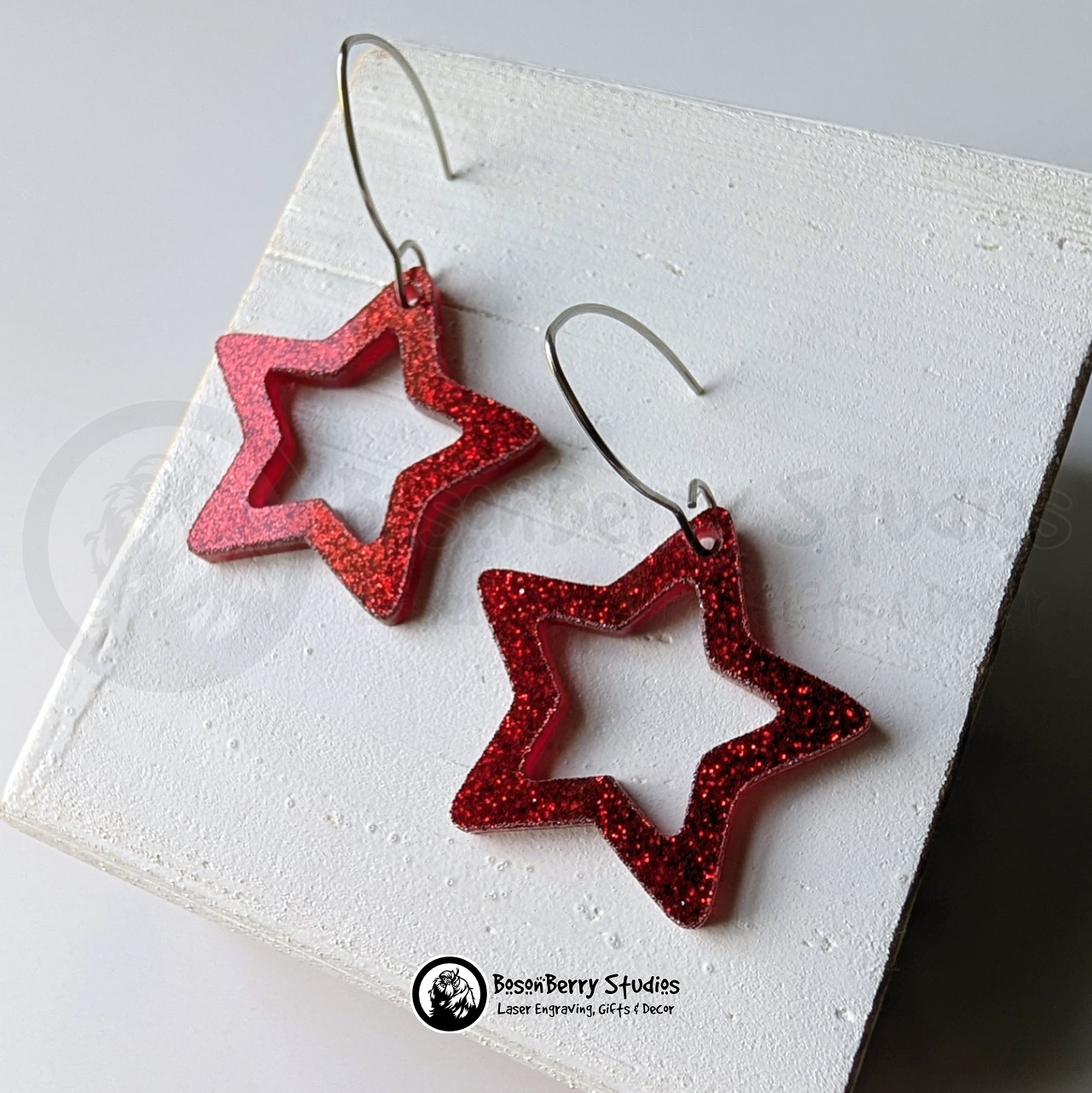 Star-shaped red glitter earrings on a white background, branded 'BosonBerry Studios'.