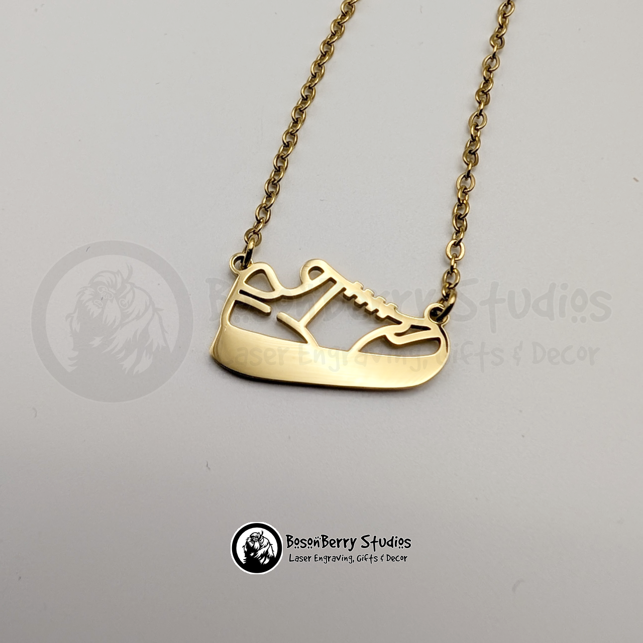 Gold necklace with a running shoe-shaped pendant on a white background with 'BosonBerry Studios' branding.