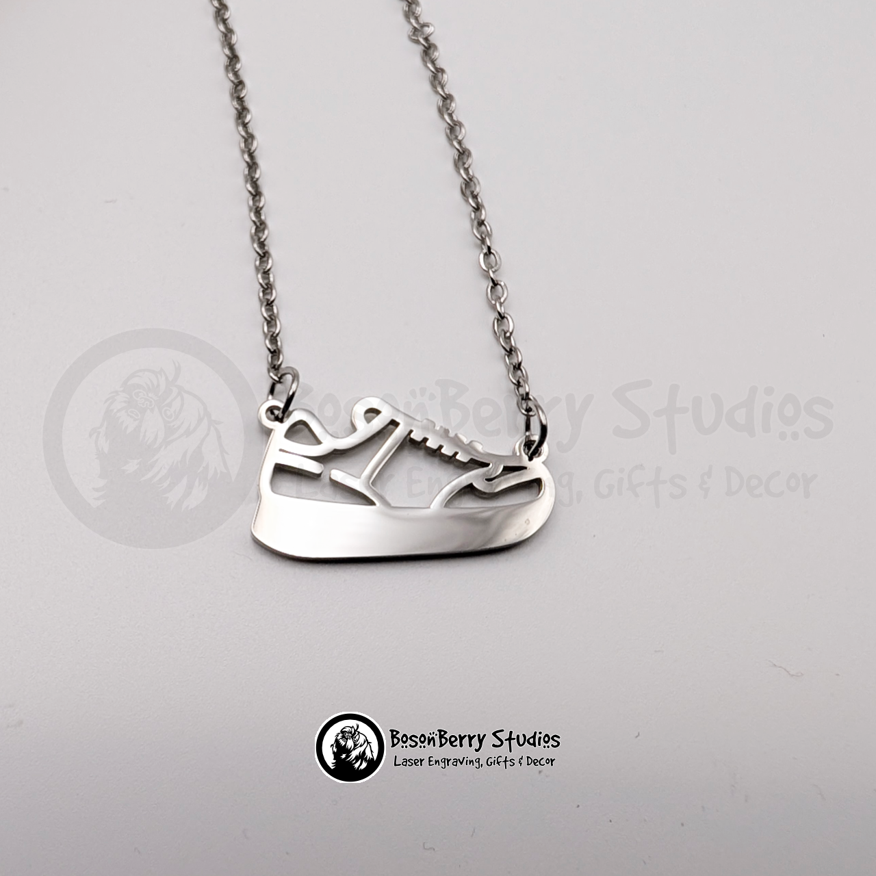 Silver necklace with a running shoe-shaped pendant on a white background with 'BosonBerry Studios' branding.