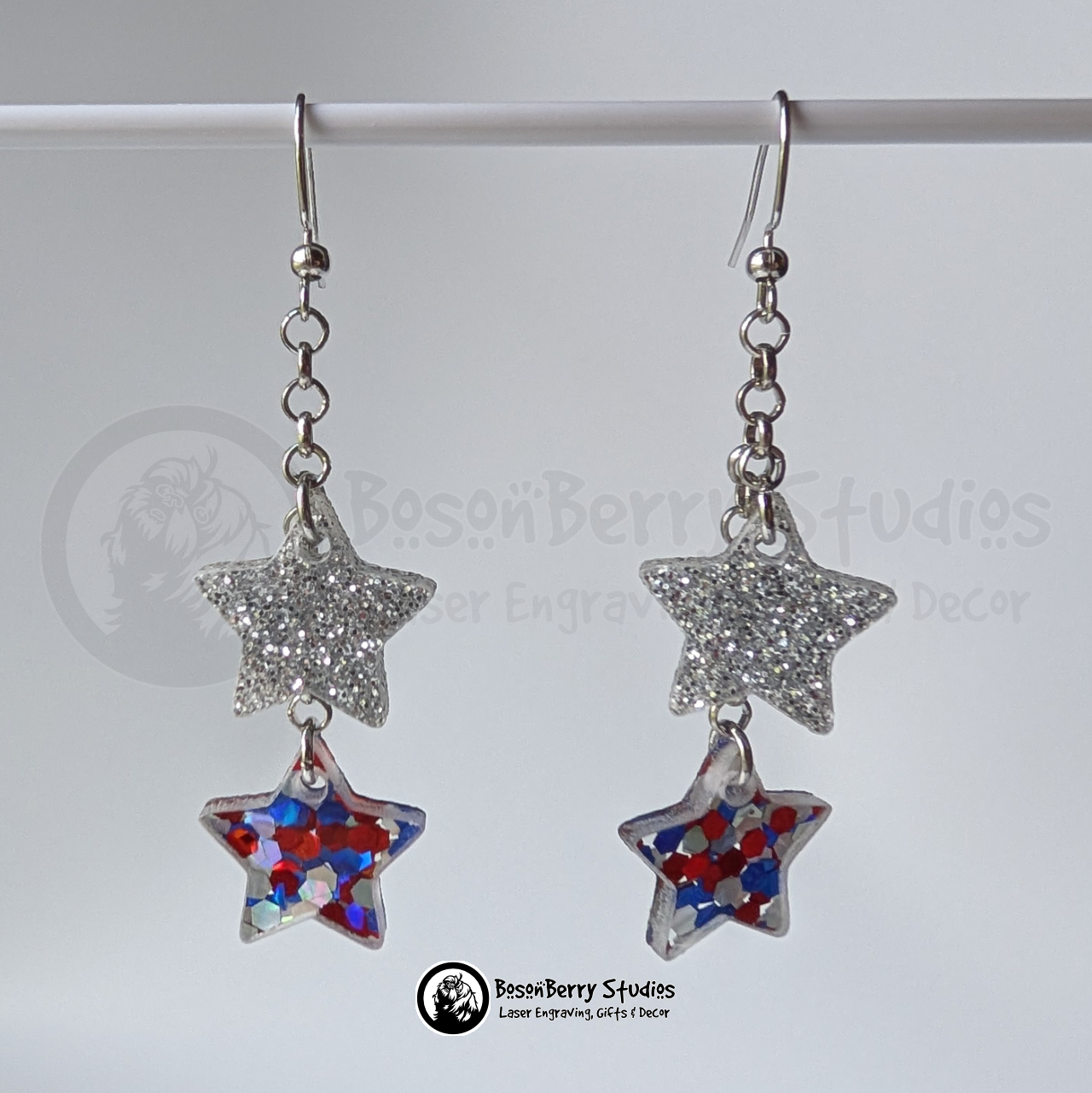 Star-shaped silver and red white blue glitter earrings suspended on a white background, branded 'BosonBerry Studios'.