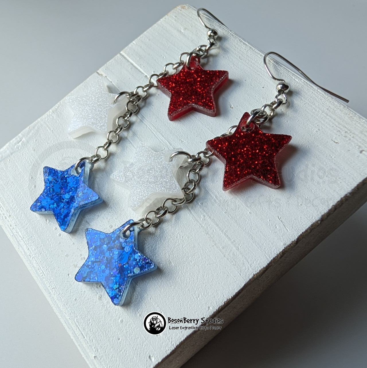 Star-shaped earrings in red, white, and blue on a white background with "BosonBerry Studios" branding.