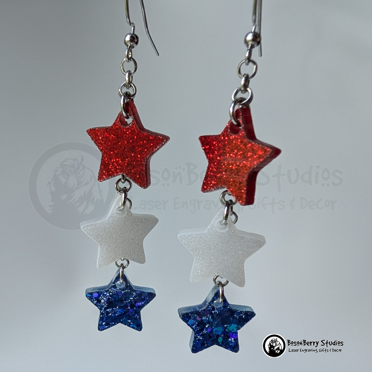 Star-shaped earrings in red, white, and blue on a white background with "BosonBerry Studios" branding.
