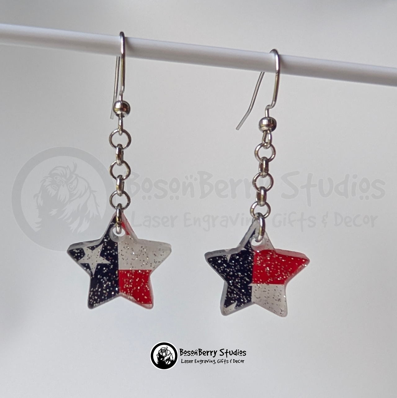 Star-shaped US flag glitter earrings suspended on a white background, branded 'BosonBerry Studios'.