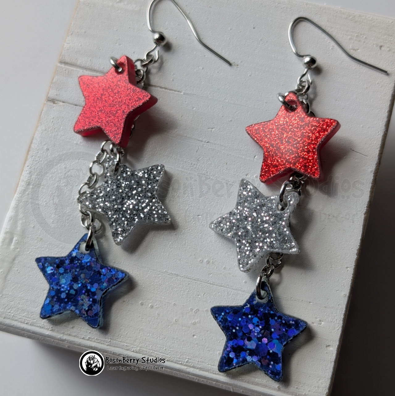 Star-shaped earrings in red, silver, and blue on a white background with "BosonBerry Studios" branding.