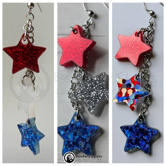 Trios of star-shaped glitter acrylic dangle earrings in red, blue, white and/or silver on a white background with BosonBerry Studios branding.