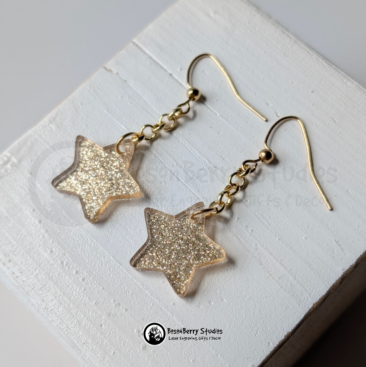 Gold star-shaped glitter dangle earrings on a white background with "BosonBerry Studios" branding.