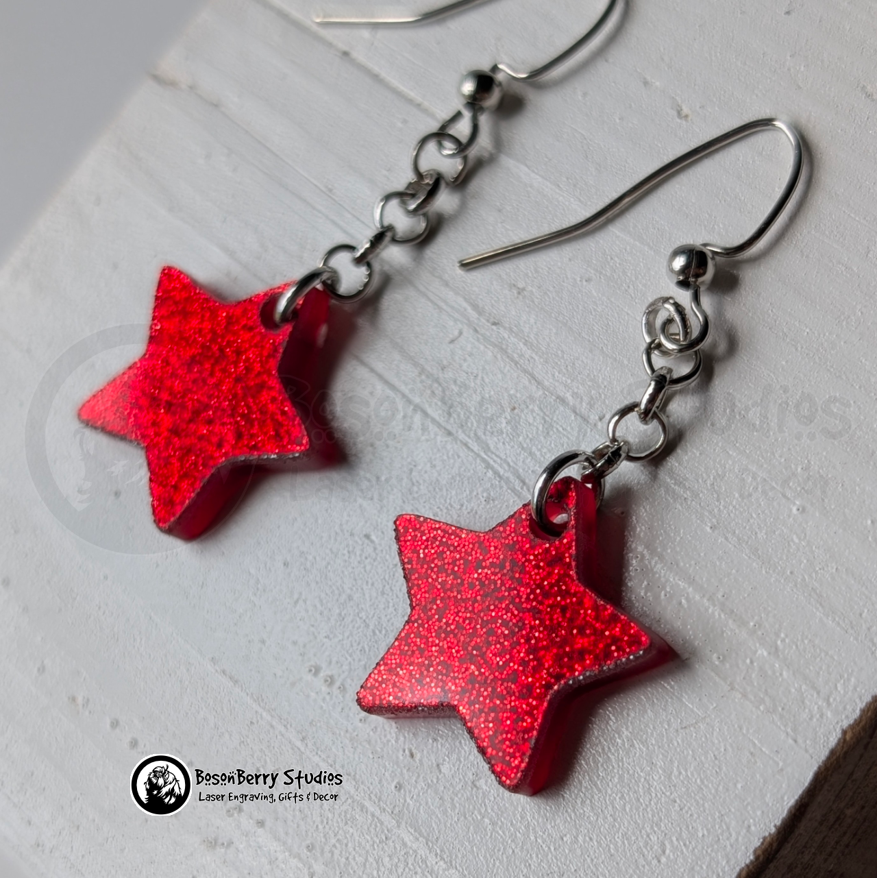 Red star-shaped glitter dangle earrings on a white background with "BosonBerry Studios" branding.