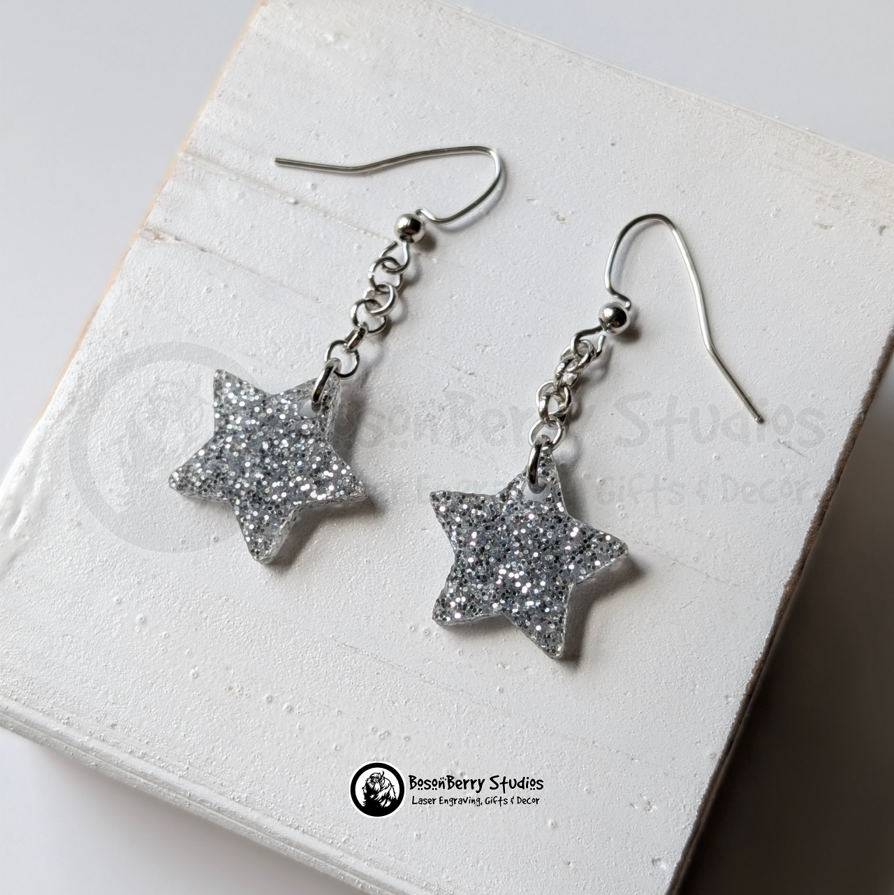 Silver star-shaped glitter dangle earrings on a white background with "BosonBerry Studios" branding.